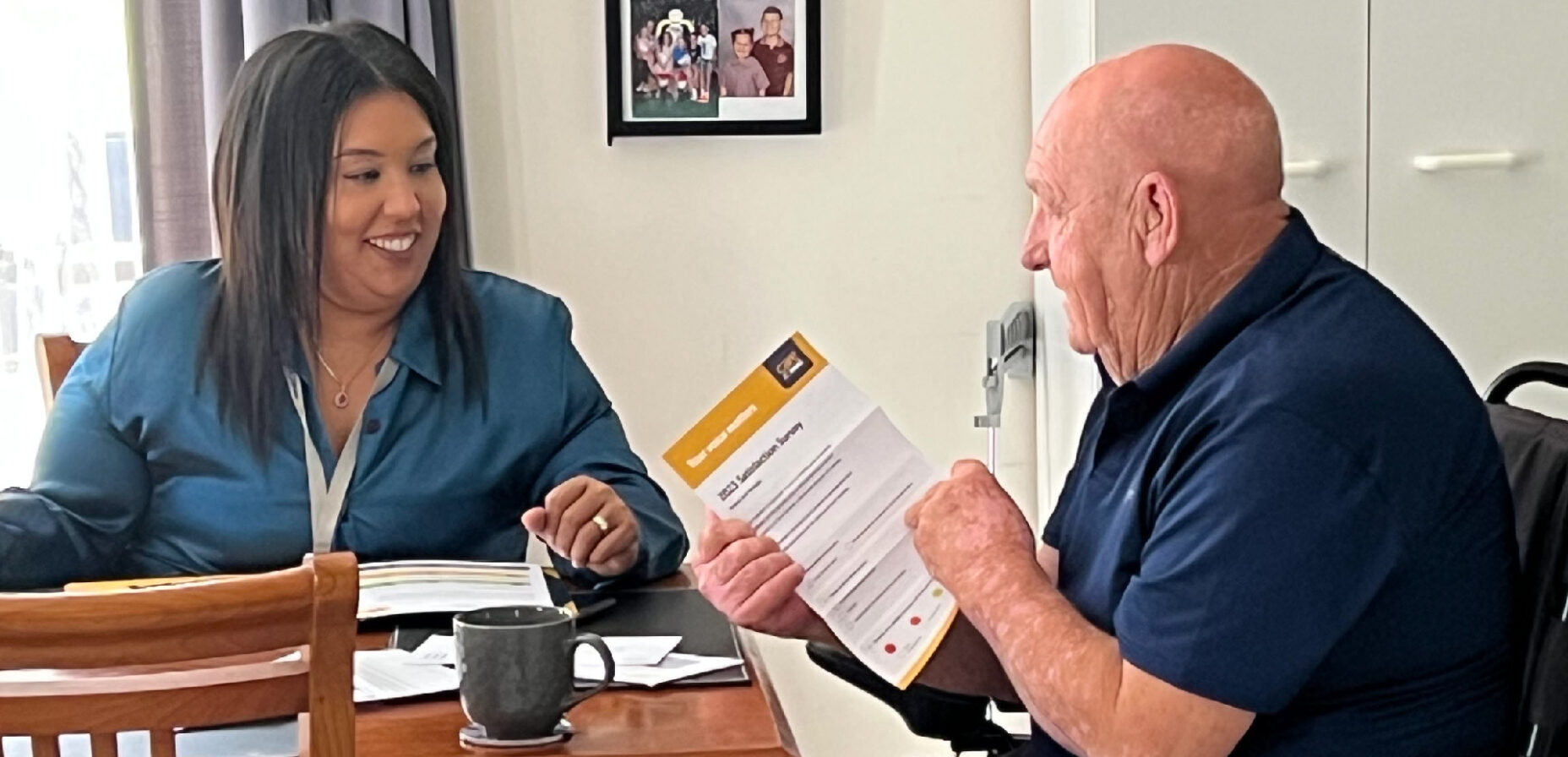 Lady with black hair sitting at a table smiling at older man who is reading a piece of paper