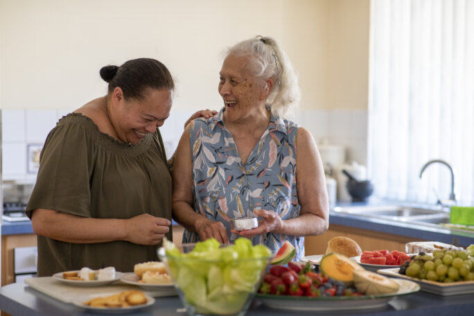 two ladies laughing with each other at a kitchen counter